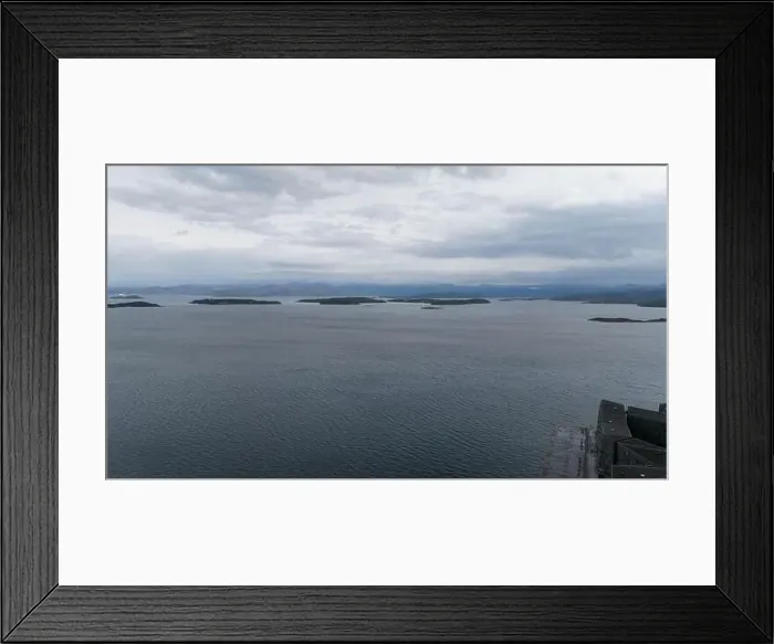 Framed Print : A serene seascape with calm waters and distant islands under a cloudy sky