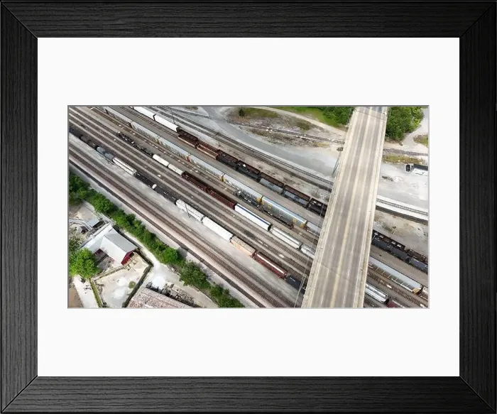Framed Print : An overhead drone shot captures the railroad tracks as a train passes through Framed Print : An overhead drone shot captures the railroad tracks as a train passes through