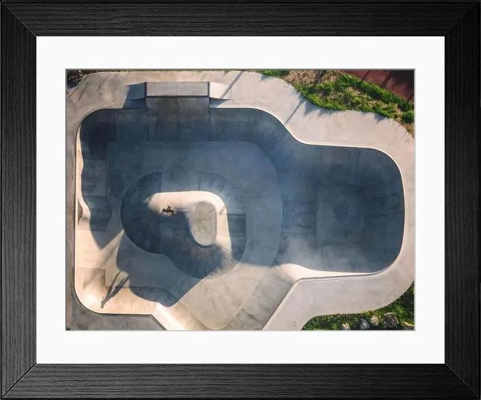 Framed Print : Aerial view of a modern skateboard park featuring diverse ramps and a skater performing tricks in the afternoon light Framed Print : Aerial view of a modern skateboard park featuring diverse ramps and a skater performing tricks in the afternoon light