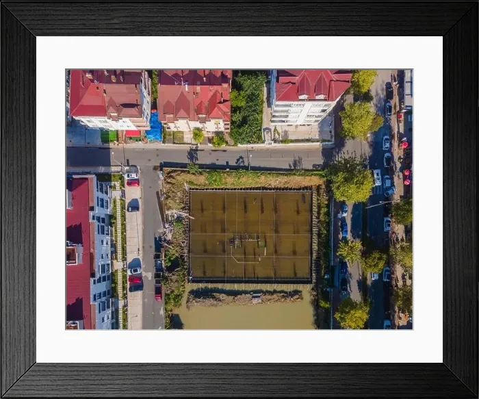 Framed Print : A city street view with a large water field in the middle. The field is surrounded by buildings and trees Framed Print : A city street view with a large water field in the middle. The field is surrounded by buildings and trees