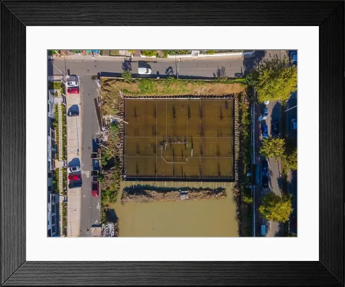 Framed Print : A city street view with a large water field in the middle. The field is surrounded by buildings and trees Framed Print : A city street view with a large water field in the middle. The field is surrounded by buildings and trees