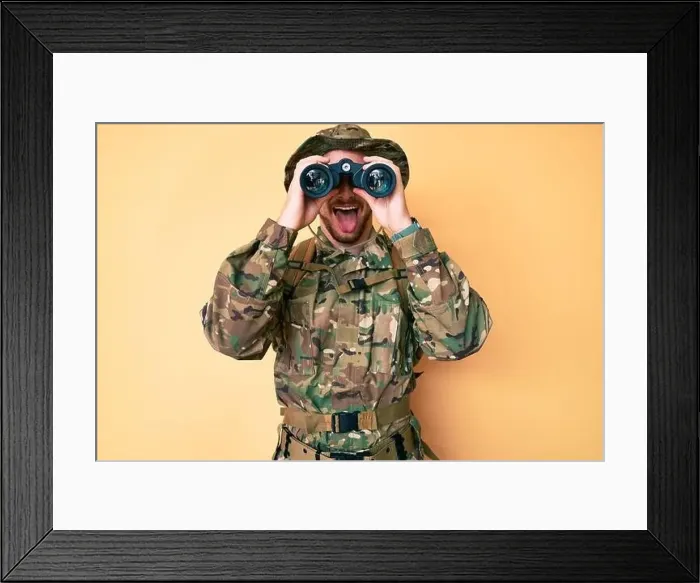 Framed Print : Young caucasian man wearing camouflage army uniform using binoculars sticking tongue out happy with funny expression