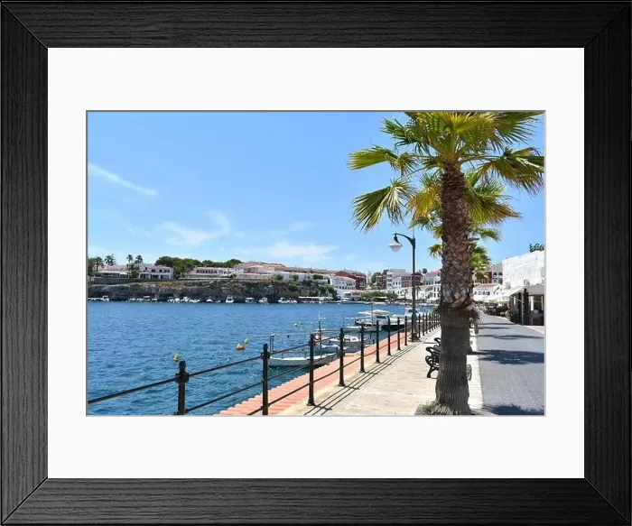 Framed Print : promenade in a village on the island of Menorca in summer sunshine, with boats and palm trees lining the road Framed Print : promenade in a village on the island of Menorca in summer sunshine, with boats and palm trees lining the road