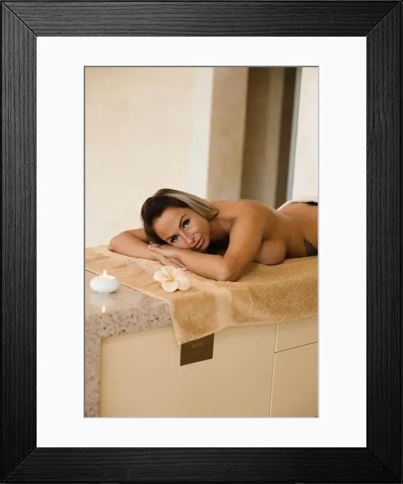Framed Print : Blonde woman relaxing in beauty salon lying on massage table with candles and aroma sticks