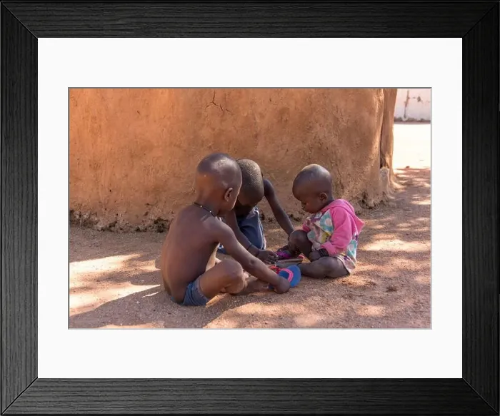 Framed Print : Three Himba children play in the shade of a mud hut Framed Print : Three Himba children play in the shade of a mud hut