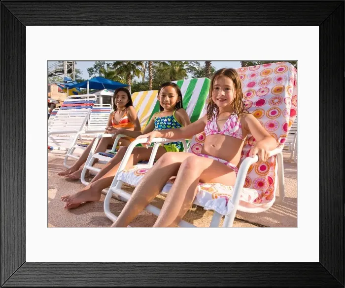 Framed Print : Multi-ethnic girls sitting on deck chairs at water park in summer Framed Print : Multi-ethnic girls sitting on deck chairs at water park in summer