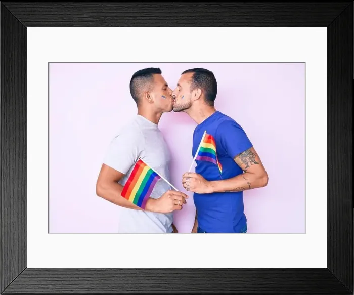 Framed Print : Young couple of gay men together in love holding homosexual pride colorful flag kissing with affection