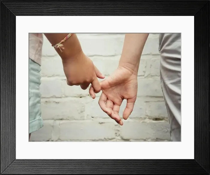 Framed Print : Two hands belonging to children, one boy and one girl, tentatively hold fingers against a white brick wall background Framed Print : Two hands belonging to children, one boy and one girl, tentatively hold fingers against a white brick wall background