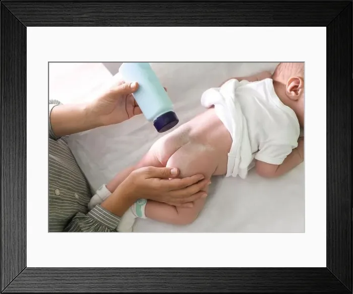 Framed Print : Mother applying dusting powder at baby's buttocks on changing table, above view Framed Print : Mother applying dusting powder at baby's buttocks on changing table, above view