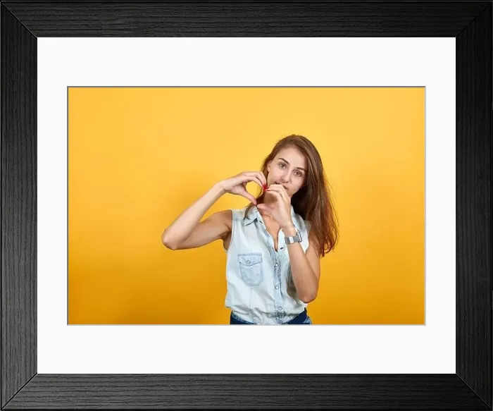 Framed Print : Attractive woman in blue denim shirt showing shape of heart gesture