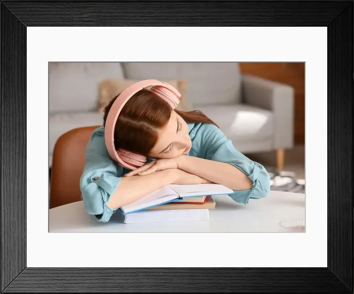 Framed Print : Tired young woman with headphones and books sleeping at table Framed Print : Tired young woman with headphones and books sleeping at table
