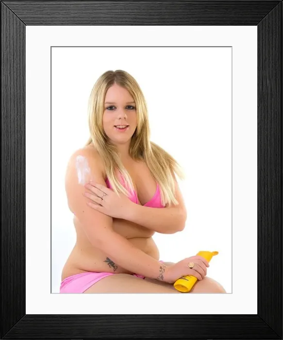 Framed Print : Attractive blonde woman wearing a bikini applys sun cream to upper arm Framed Print : Attractive blonde woman wearing a bikini applys sun cream to upper arm