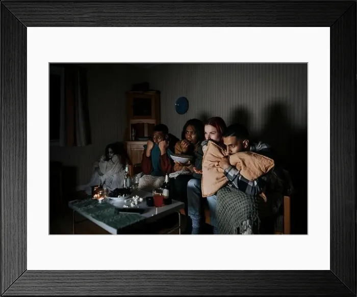Framed Print : Frightened multiracial friends watching scary movie while ghost sitting in corner at cabin