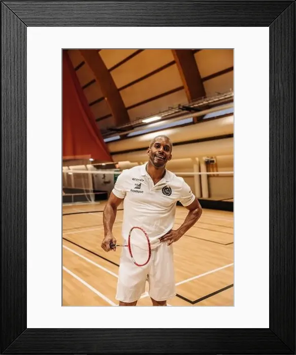 Framed Print : Male badminton player standing with hand on hip while holding racket at sports court