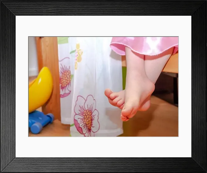 Framed Print : Close-up of little girl feet while sitting on bed Framed Print : Close-up of little girl feet while sitting on bed