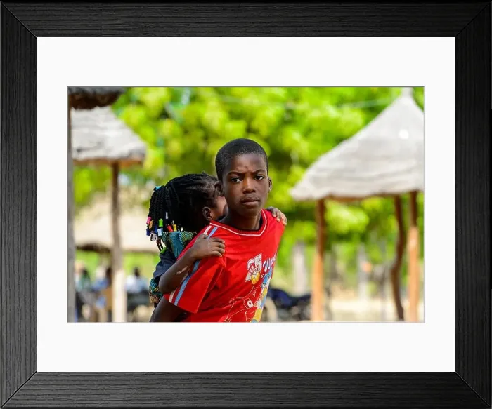 Framed Print : KOUTAMMAKOU, TOGO - JAN 13, 2017: Unidentified Togolese boy in red shirt carries his little sister in the village Framed Print : KOUTAMMAKOU, TOGO - JAN 13, 2017: Unidentified Togolese boy in red shirt carries his little sister in the village