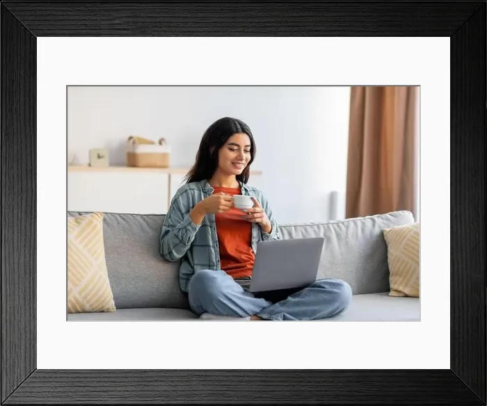 Framed Print : Full length of beautiful young Arab woman sitting cross legged on couch, working on laptop, drinking coffee at home Framed Print : Full length of beautiful young Arab woman sitting cross legged on couch, working on laptop, drinking coffee at home