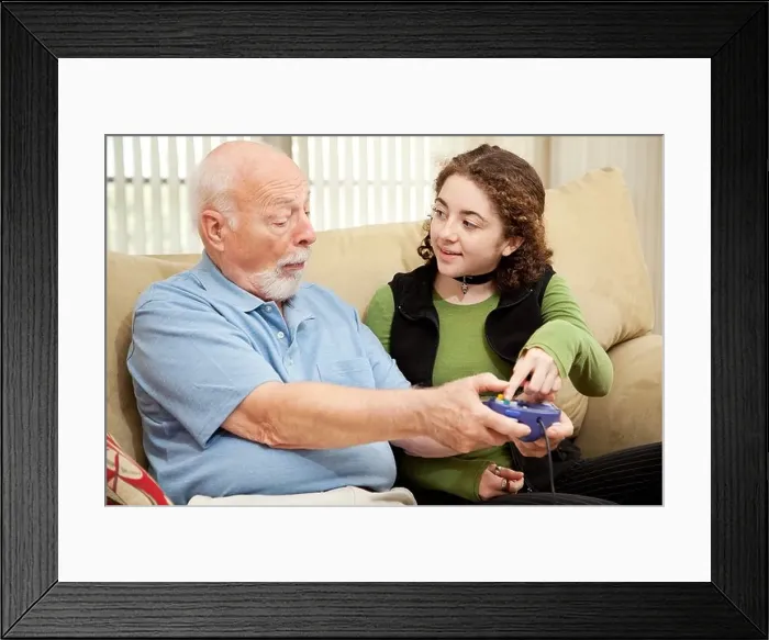 Framed Print : Teen girl teaching her grandfather how to play video games Framed Print : Teen girl teaching her grandfather how to play video games