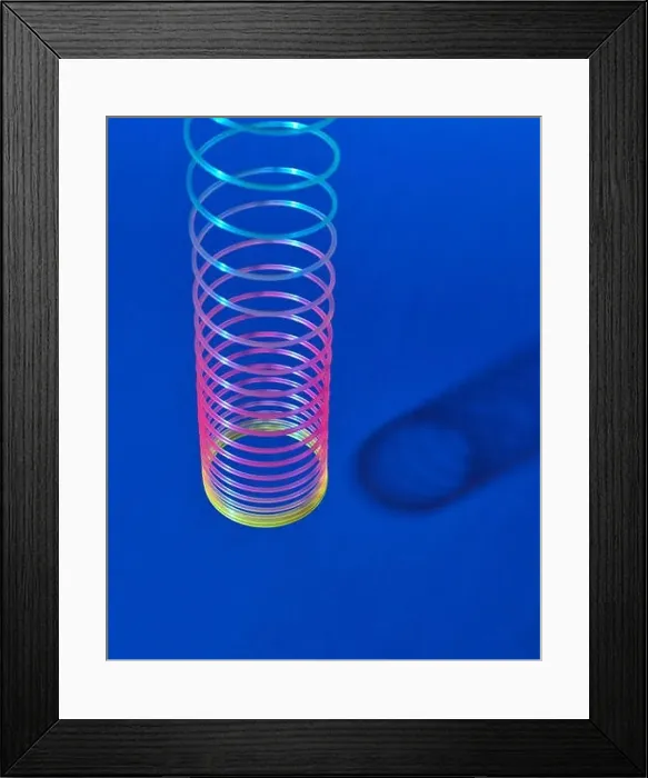 Framed Print : Stretching rainbow plastic slinky toy above blue background with shadows, place for text Framed Print : Stretching rainbow plastic slinky toy above blue background with shadows, place for text