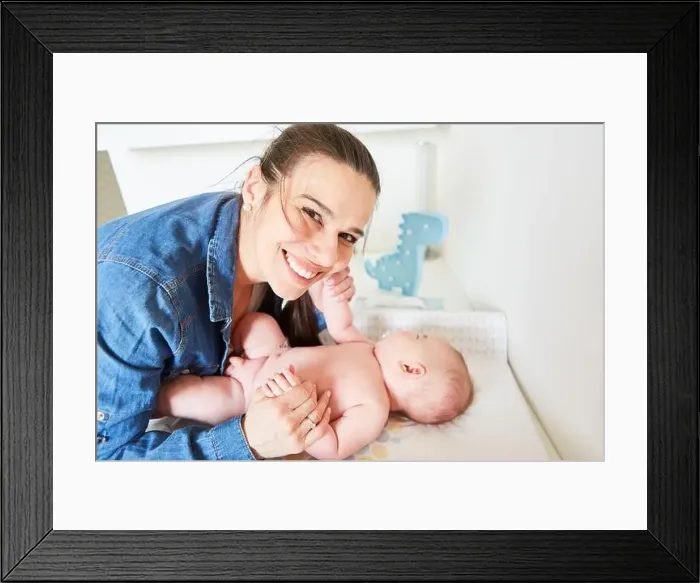 Framed Print : Happy mother lovingly holds her baby by the hands while caring for it on the changing table Framed Print : Happy mother lovingly holds her baby by the hands while caring for it on the changing table