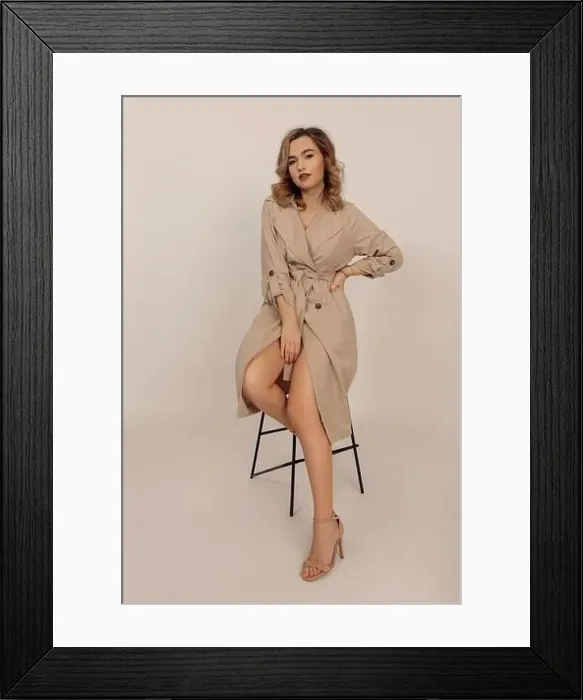 Framed Print : Portrait of young beautiful woman with professional make-up and long wavy hair sitting on chair in beige trench coat Framed Print : Portrait of young beautiful woman with professional make-up and long wavy hair sitting on chair in beige trench coat