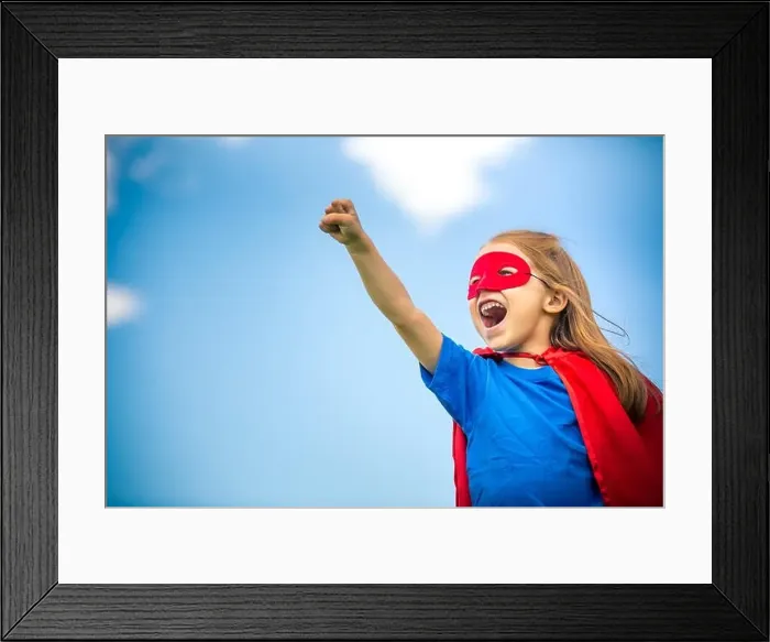 Framed Print : Funny little girl playing power super hero over blue sky background. Superhero concept Framed Print : Funny little girl playing power super hero over blue sky background. Superhero concept