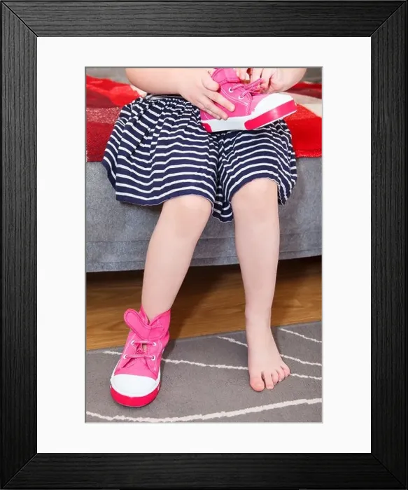Framed Print : Small girl wearing pink shoes on leg sitting on sofa in domestic room Framed Print : Small girl wearing pink shoes on leg sitting on sofa in domestic room
