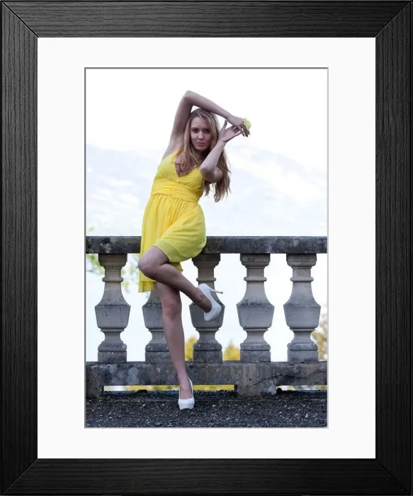 Framed Print : Young woman posing in a yellow dress with white high heels in front of a balustrade Framed Print : Young woman posing in a yellow dress with white high heels in front of a balustrade