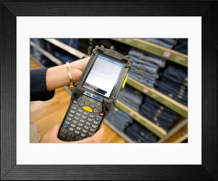 Framed Print : A sales associate uses a Telxon handheld scanner to read EPC / RFID labels on clothing at a Walmart Supercenter in Rogers Framed Print : A sales associate uses a Telxon handheld scanner to read EPC / RFID labels on clothing at a Walmart Supercenter in Rogers