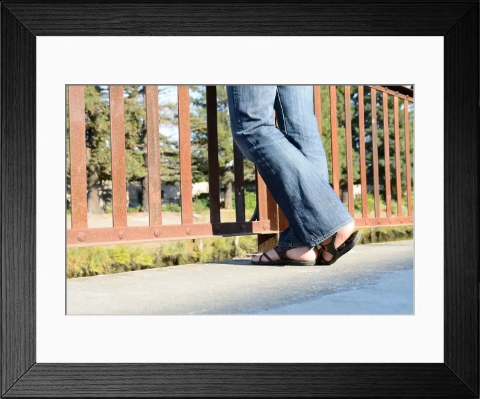 Framed Print : Womans legs and feet standing by a fence wearing jeans and sandals Framed Print : Womans legs and feet standing by a fence wearing jeans and sandals