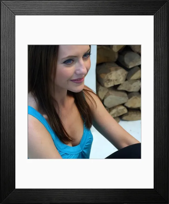 Framed Print : Smiling young woman beside a fireplace stacked with logs Framed Print : Smiling young woman beside a fireplace stacked with logs