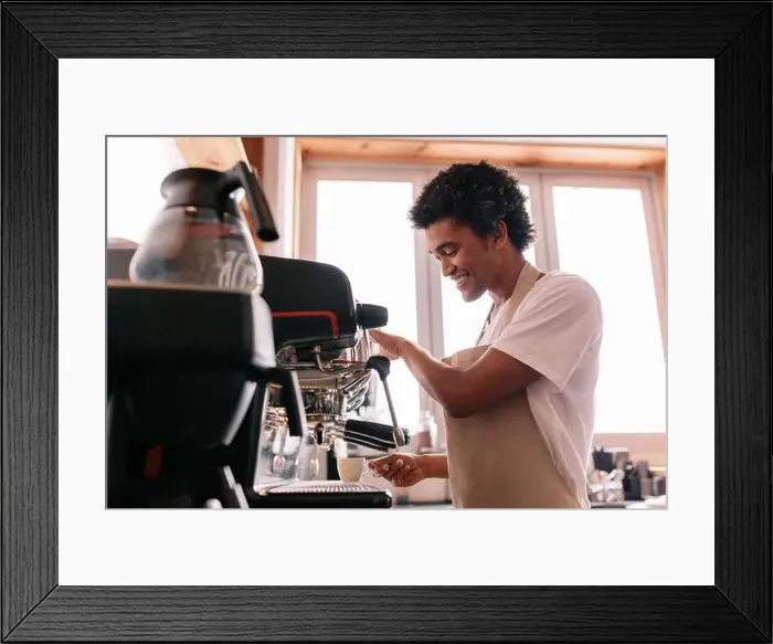 Framed Print : Professional barista holding cup on the coffee machine. Young man making coffee with an espresso coffee machine at cafe