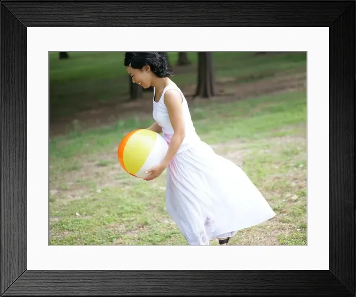 Framed Print : Side profile of a young woman holding a beach ball in a park Framed Print : Side profile of a young woman holding a beach ball in a park
