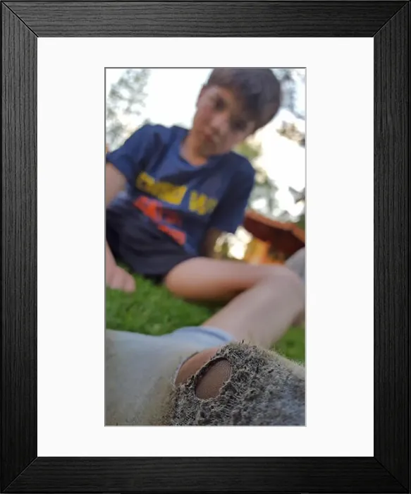 Framed Print : boy sitting on the lawn and looking at his dirty sock full of holes Framed Print : boy sitting on the lawn and looking at his dirty sock full of holes