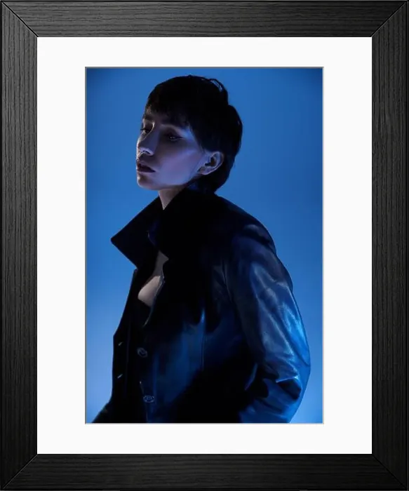 Framed Print : Young woman striking a pose in a black leather jacket against a vibrant blue backdrop Framed Print : Young woman striking a pose in a black leather jacket against a vibrant blue backdrop