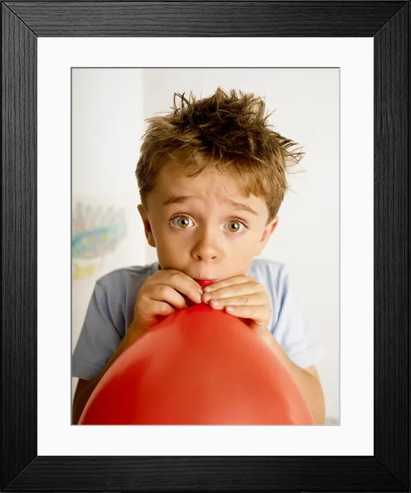 Framed Print : boy 7 blowing up a red balloon for a birthday party looking wide eyed Framed Print : boy 7 blowing up a red balloon for a birthday party looking wide eyed
