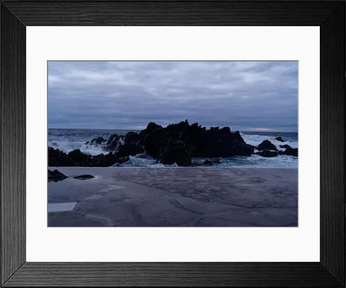 Framed Print : Waves crash against volcanic rocks under a dramatic sky at Porto Moniz natural pools Framed Print : Waves crash against volcanic rocks under a dramatic sky at Porto Moniz natural pools