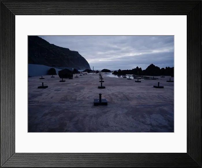 Framed Print : Empty parasol stands line the moody coastline at Porto Moniz natural pools, with towering cliffs in the background Framed Print : Empty parasol stands line the moody coastline at Porto Moniz natural pools, with towering cliffs in the background