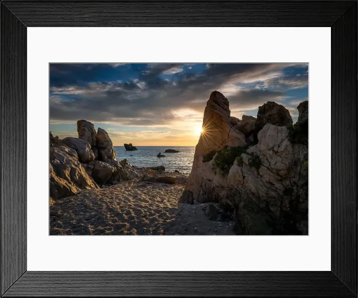 Framed Print : A rocky beach with the sun setting over the sea casting highlights on the sky clouds and sun ray peeping behind a rock Framed Print : A rocky beach with the sun setting over the sea casting highlights on the sky clouds and sun ray peeping behind a rock