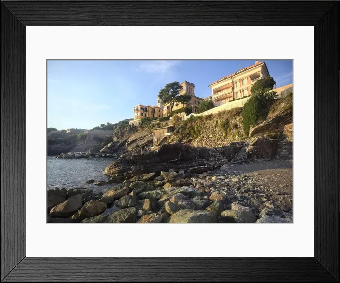 Framed Print : Town buildings on a cliff facing the sea at sunset seen from a cove Framed Print : Town buildings on a cliff facing the sea at sunset seen from a cove