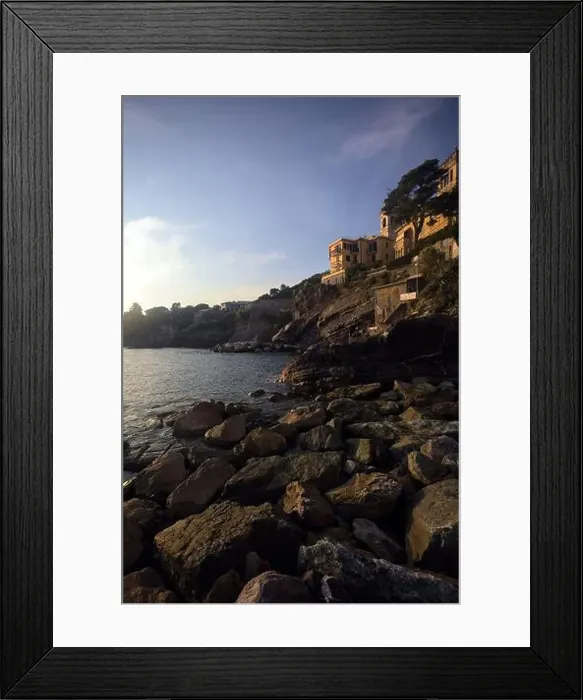Framed Print : Town buildings on a cliff facing the sea at sunset seen from a cove Framed Print : Town buildings on a cliff facing the sea at sunset seen from a cove