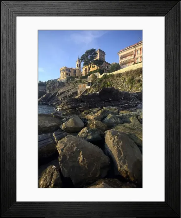 Framed Print : Town buildings on a cliff facing the sea at sunset seen from a cove Framed Print : Town buildings on a cliff facing the sea at sunset seen from a cove