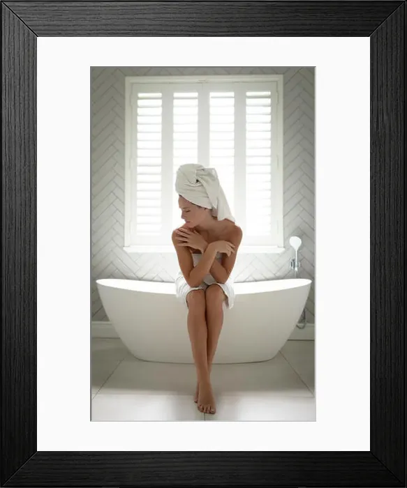 Framed Print : Woman sitting on the edge of bathtub and embracing self