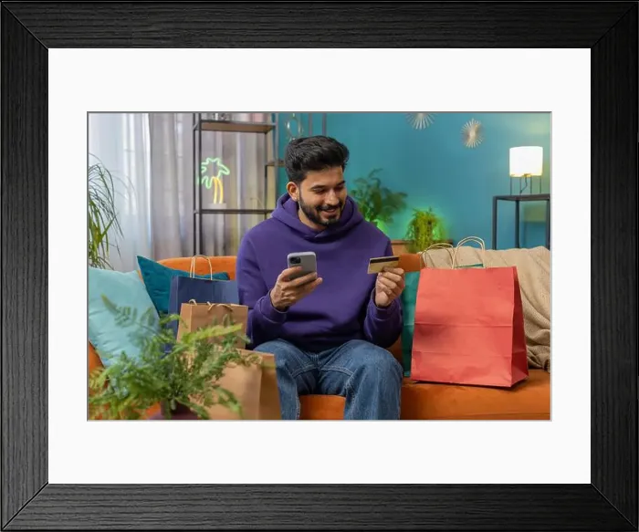 Framed Print : Happy shopaholic consumer indian man sitting with shopping bags at modern home apartment making online order Framed Print : Happy shopaholic consumer indian man sitting with shopping bags at modern home apartment making online order
