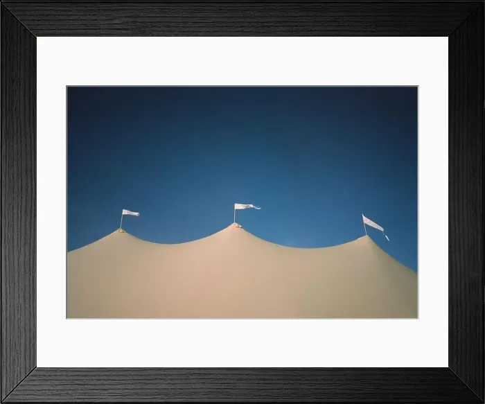 Framed Print : A low angle shot of three white flags waving in the wind on top of a medieval-style tent under a blue sky Framed Print : A low angle shot of three white flags waving in the wind on top of a medieval-style tent under a blue sky