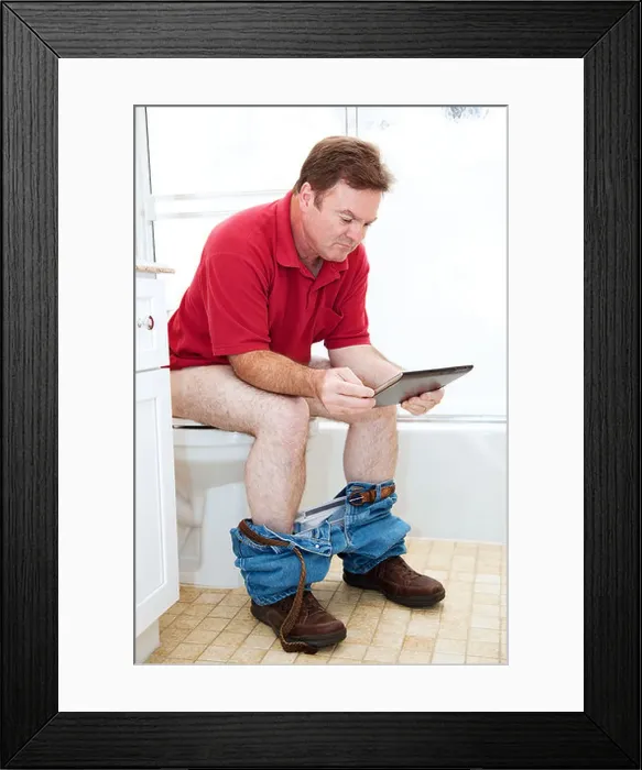 Framed Print : Man reading a tablet pc while using the toilet in the bathroom Framed Print : Man reading a tablet pc while using the toilet in the bathroom