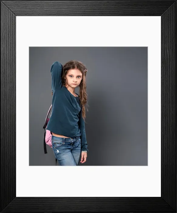 Framed Print : Thinking pupil kid gilr posing in style clothing and holding backpack on grey studio background. Closeup