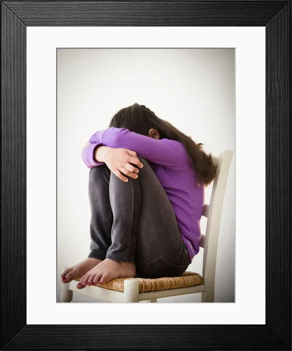 Framed Print : Studio shot of sad girl (8-9) curling on chair Framed Print : Studio shot of sad girl (8-9) curling on chair