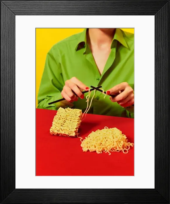 Framed Print : Creative image with woman knitting instant noodles on blue table on vivid red tablecloth over yellow background