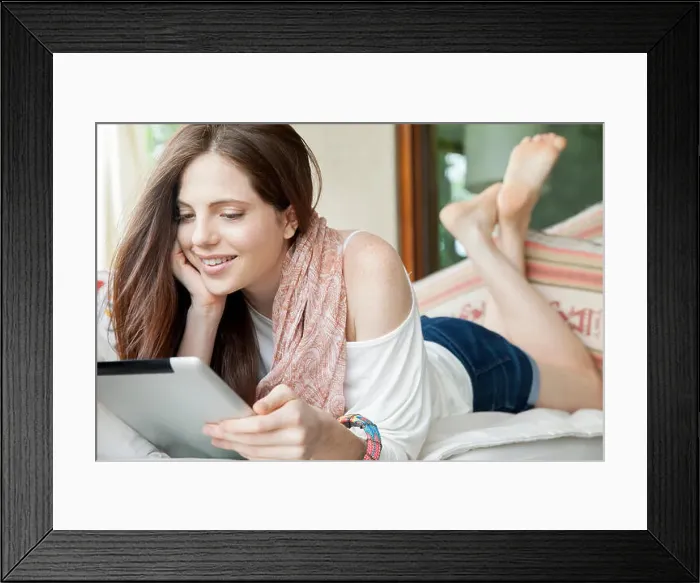 Framed Print : Young woman lying on stomach, looking at digital tablet